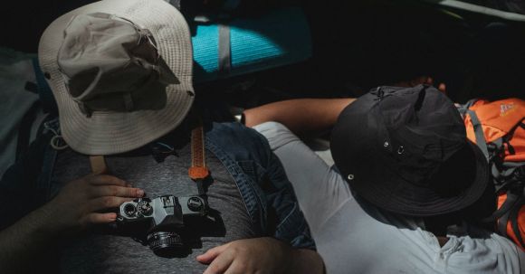 Sleep Exploration - From above unrecognizable males in casual clothes covering faces with hats and sleeping in tent after long hiking